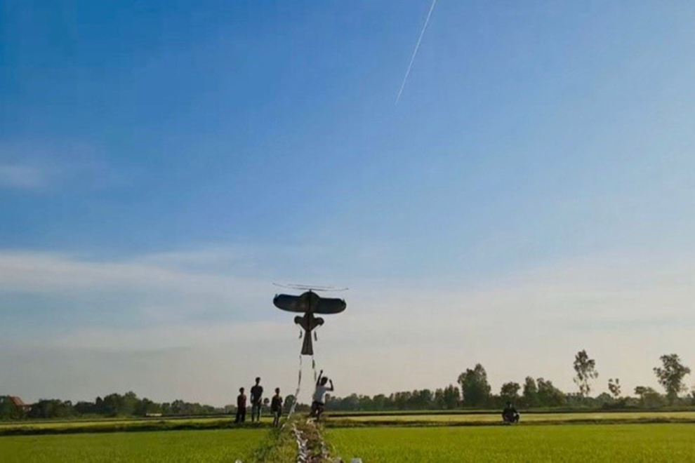 Young people launch their Kleng Ek kites high above a rice paddy. Supplied