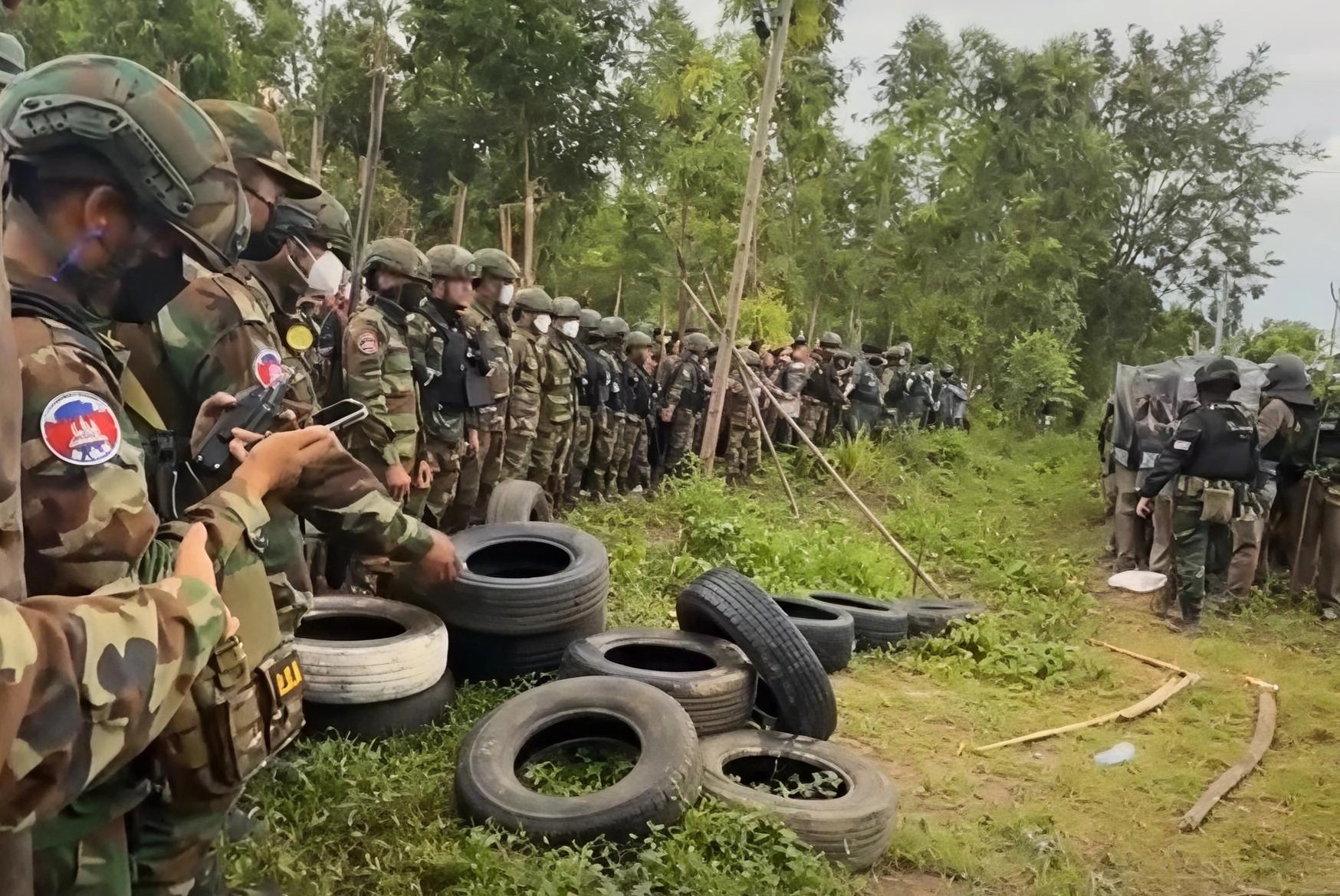 Unarmed Cambodian soldiers stand guard while Thai forces deploy with body armour and riot shield. Supplied