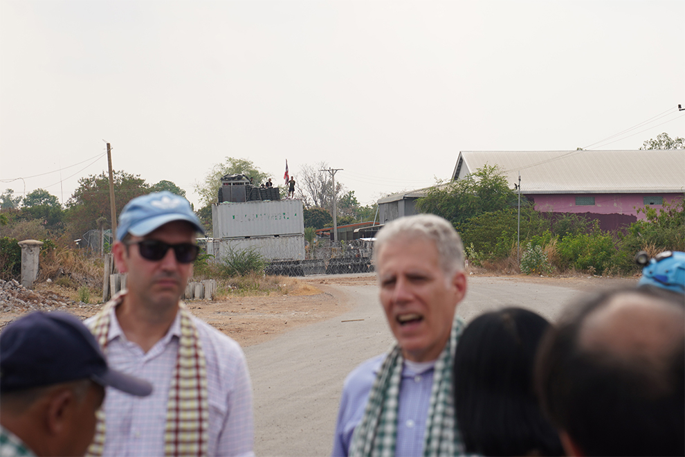 Diplomats and NGO representatives listen to the governor of Banteay Meanchey province. Thai shipping container barricades are visible in the background. Hong Raksmey
